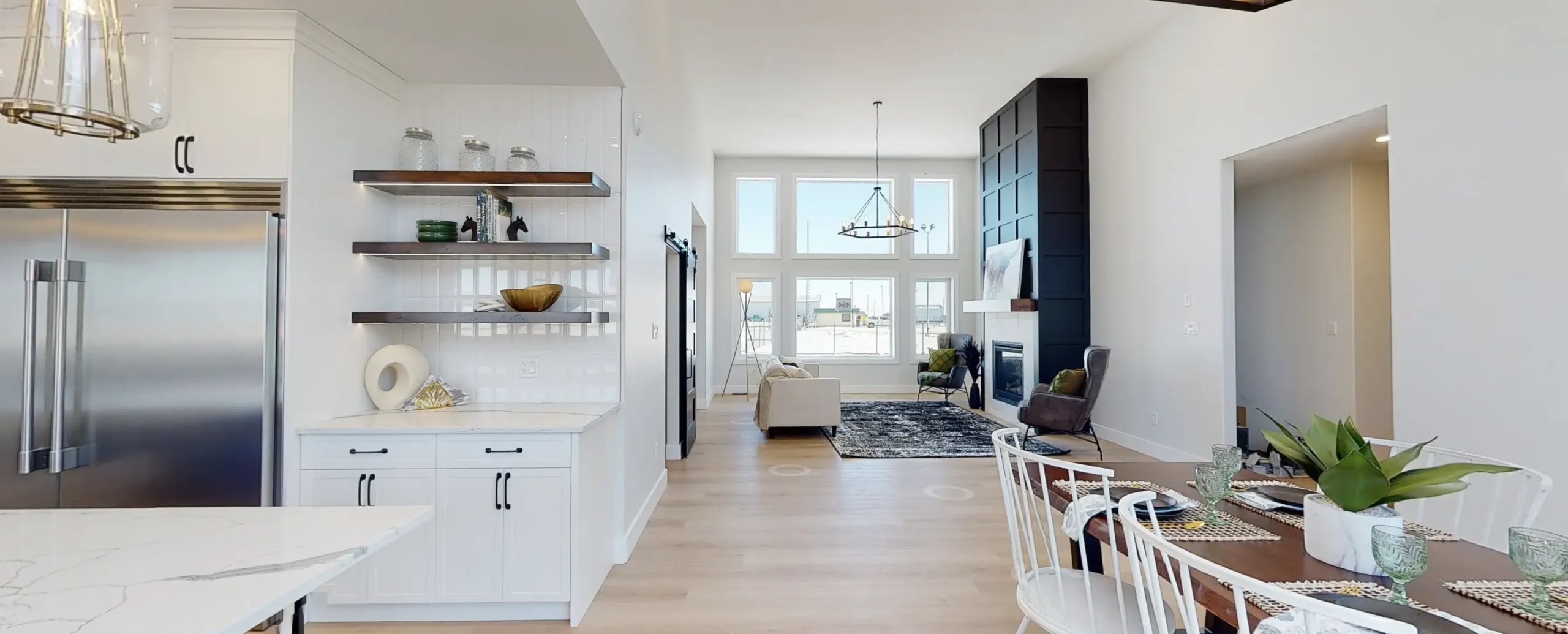 Open concept RTM home in Alberta or Saskatchewan with bright grid windows, black feature fireplace wall, dining area, and white kitchen shelving.